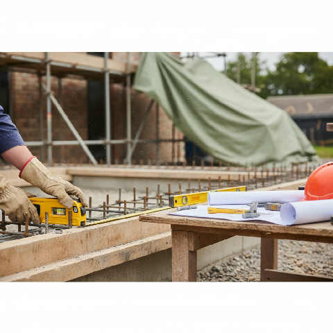 A technician uses a digital leveling tool on a bright construction site while holding a clipboard and technical plans.