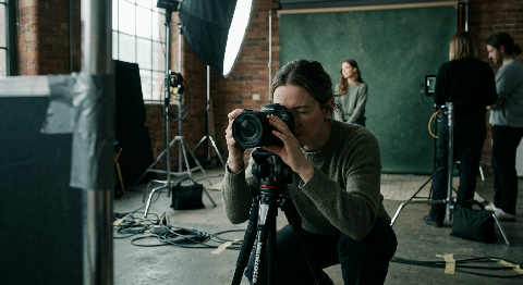 A photographer adjusts a lighting rig in a dark studio while viewing a product shoot on a tethered monitor.
