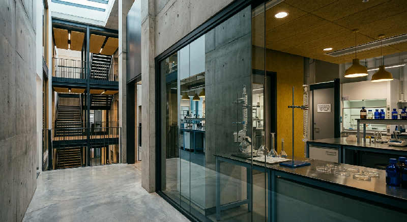 Polished concrete floor reflecting a tall minimalist window and structured industrial beams in a moody interior.