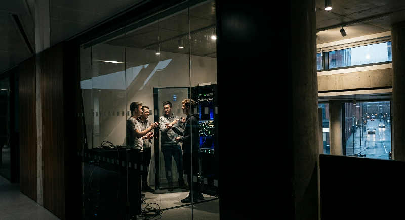 A blurred person walks through a modern glass building, reflected in a polished wall with bright architectural lighting.